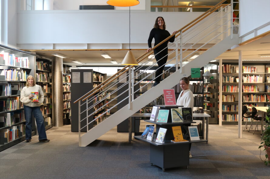 Tre kvinner står inne i et bibliotek.