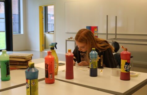 Billedbøker med vekt på det sanselige To studenter jobber ved et bord fylt med fargesprutflasker og pensler i et lyst kunstlokale.