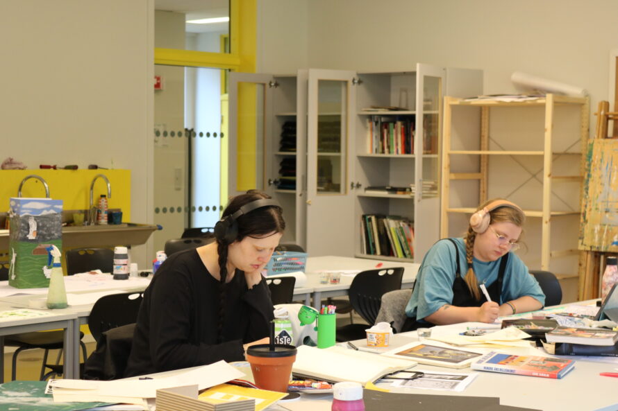 To personer sitter ved et arbeidsbord, arbeider med tegninger og trykk.