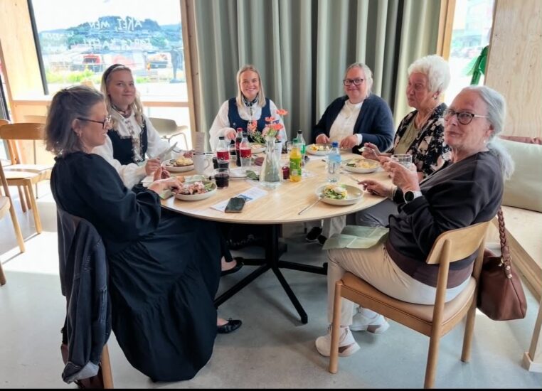 6 personer sitter rundt et rundt bord og spiser.