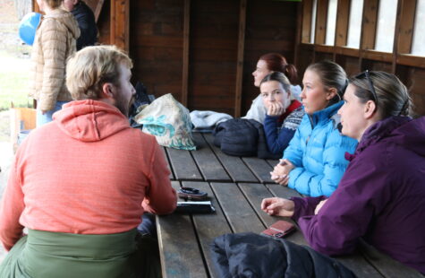 Noen unge mennesker sitter inne i et trebygg, vi kan skimte dagslys utenfor