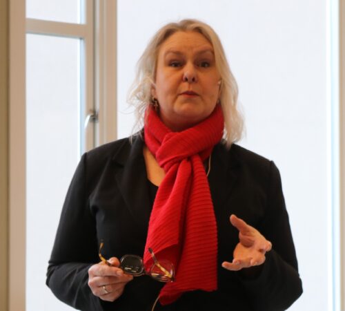 EN kvinne med rødt skjerf holder brillene sine i hånden.