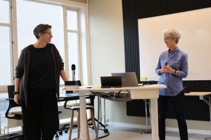 To kvinner i et klasserom prater til hverandre.