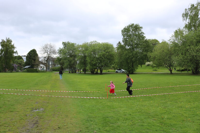 Et barn og en voksen løper etter hverandre i en park.
