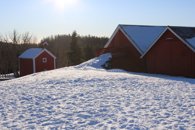 Bilde av en gård med snø rundt. Sola skinner