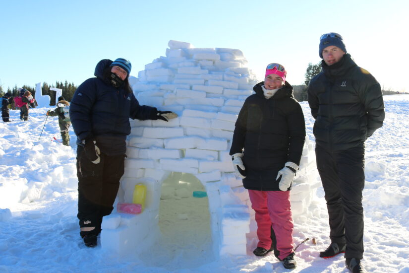 3 unge mennesker står foran en iglo de har bygd selv.
