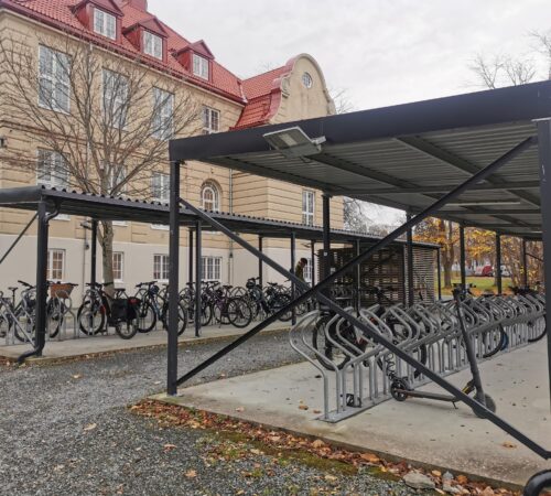 Bilde av sykkelparkeringen fra utsiden. I bakgrunnen ser vi hovedbygget.