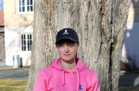 Hettegenser rosa Bilde av en student i en rosa DMMH hettegenser foran et tre i parken foran hovedbygget.