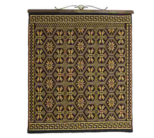 Bilde av vev utført i sort og gul oker med ornamenter. 78 x 91 cm. Plassert ved korridor i mellombygg ved toalett 2. etasje.