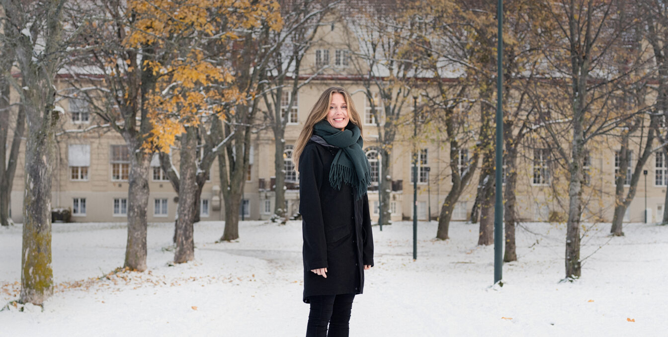 Smilende kvinnelig ansatt foran administrasjonsbygget på vinteren