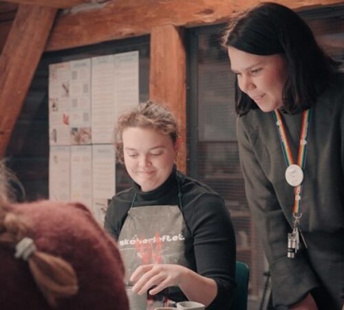 Bilde av student som jobber kreativt mens lærer ser på