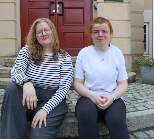 To unge kvinner sitter på trappa foran DMMH.
