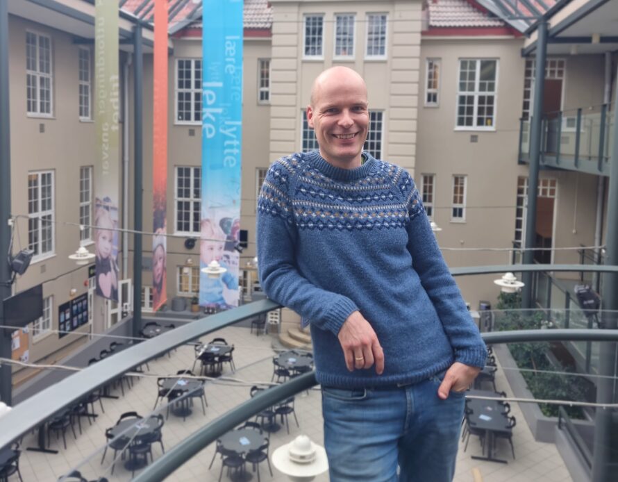 Høgskolelektor Tormod Murud-Riser lener som mot et gelender og smiler i Glassgården.