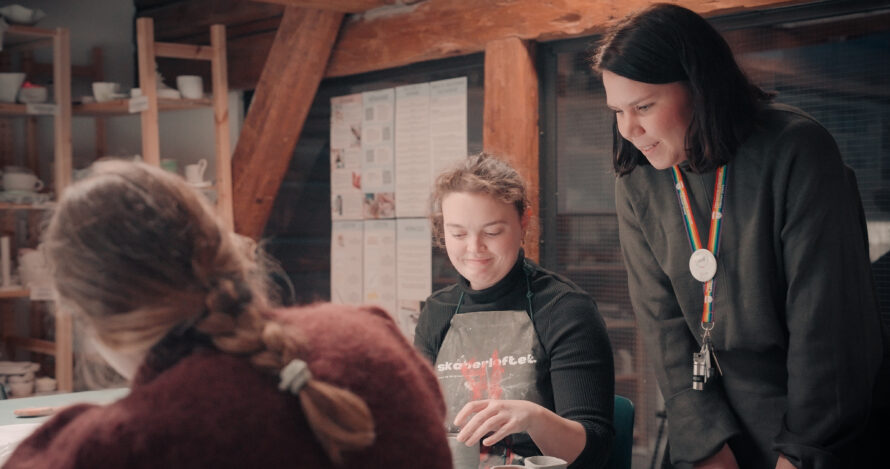 En voksen dame snakker med to to unge jenter som sitter ved et bord.