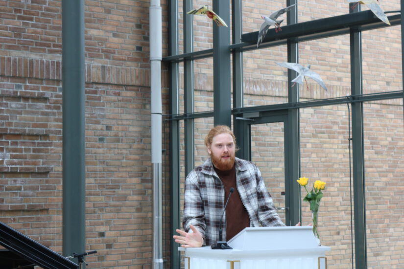 En ung mann står ved en talerstol med 3 gule roser.