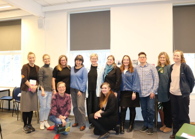 En gruppe kvinner og en mann står oppstilt i to rader foran en vegg.