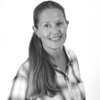 Smiling woman with long hair in a plaid shirt, facing slightly to the right, against a plain light background.