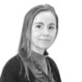 Nærbilde av en person med skulderlangt ligger. Personen har lyst hår, svarer rolig til venstre, iført svart cardigan og mønstret skjorte i loddrett mønster.